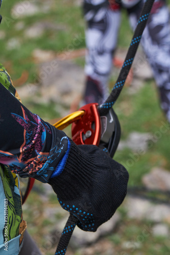 Detailed shot of a climber's hand handling a belay device and rope, ready to ascend.