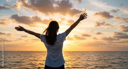 Woman with arms outstretched enjoying sunset over ocean, symbolizing freedom and happiness