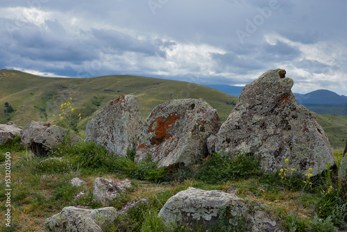 Scenic view of lush green hills and dramatic red cliffs under a bright blue sky with white clouds, showcasing the beauty of untouched mountainous nature and diverse rocky terrain.