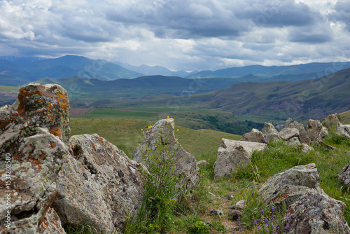 Scenic view of lush green hills and dramatic red cliffs under a bright blue sky with white clouds, showcasing the beauty of untouched mountainous nature and diverse rocky terrain.