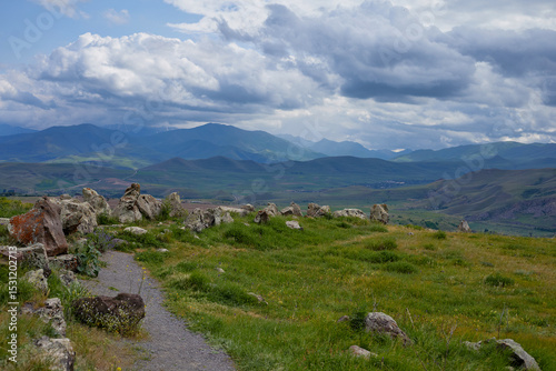 Scenic view of lush green hills and dramatic red cliffs under a bright blue sky with white clouds, showcasing the beauty of untouched mountainous nature and diverse rocky terrain.
