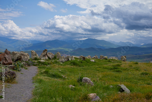 Scenic view of lush green hills and dramatic red cliffs under a bright blue sky with white clouds, showcasing the beauty of untouched mountainous nature and diverse rocky terrain.