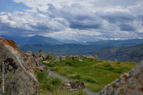 Scenic view of lush green hills and dramatic red cliffs under a bright blue sky with white clouds, showcasing the beauty of untouched mountainous nature and diverse rocky terrain.
