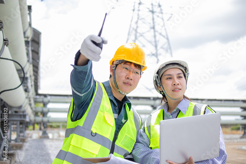 Two engineers working at power station are inspecting equipment with focus and determination while wearing safety helmets and reflective vests in industrial outdoor setting
