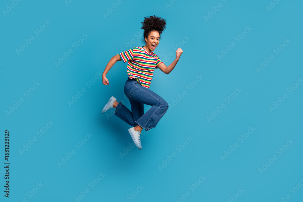 Fotografie Cheerful young woman jumping joyfully against a solid turquoise background, expr