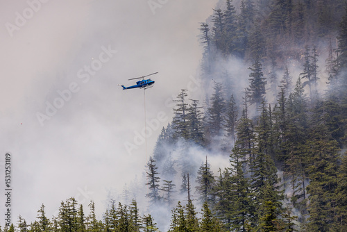Helicopter Extinguishing a Forest Fire in a Mountainous Terrain Amidst Heavy Smoke