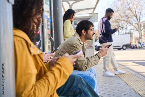 multiethnic people using smartphones while waiting at bus stop