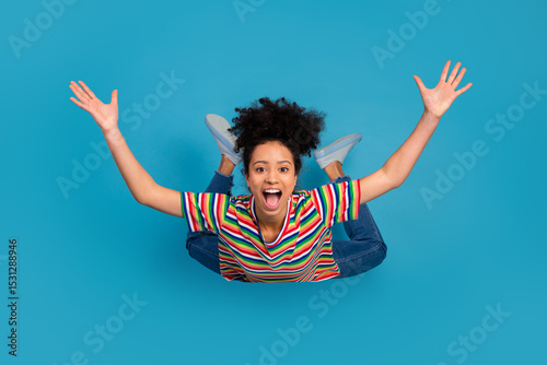 Young cheerful woman in a colorful striped t-shirt posing against a vibrant blue background with joyful excitement