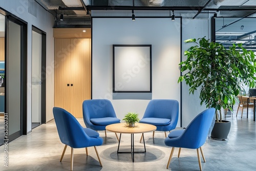Modern, minimalist office waiting area with four blue armchairs arranged around a small, round table.  A blank canvas hangs on a white wall.  Plants and natural light enhance the space