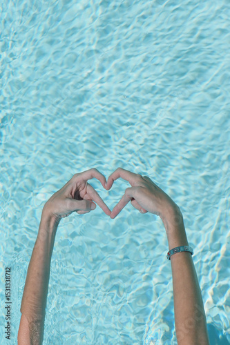 Hands creating a heart shape in swimming pool.
