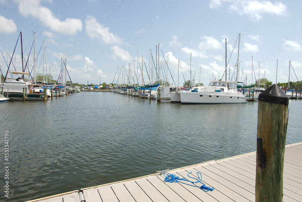 Fototapeta premium Tranquil Marina with Boats Moored Under a Clear Blue Sky. Gulfport, FL. Boats and yachts moored peacefully, under a bright blue sky with wispy white clouds, exemplifying a coastal lifestyle and scenic