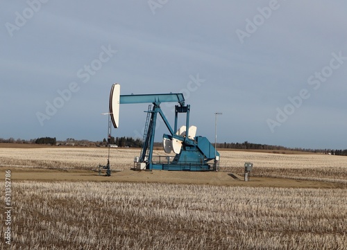 A blue or teal colored pumpjack in an Alberta prairie grain field. Pumping oil into a pipeline to take it to a refinery or for export.