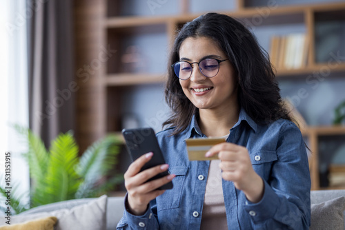 Photography Close-up photo of a young Indian woman sitting on the sofa at home, holding a cr