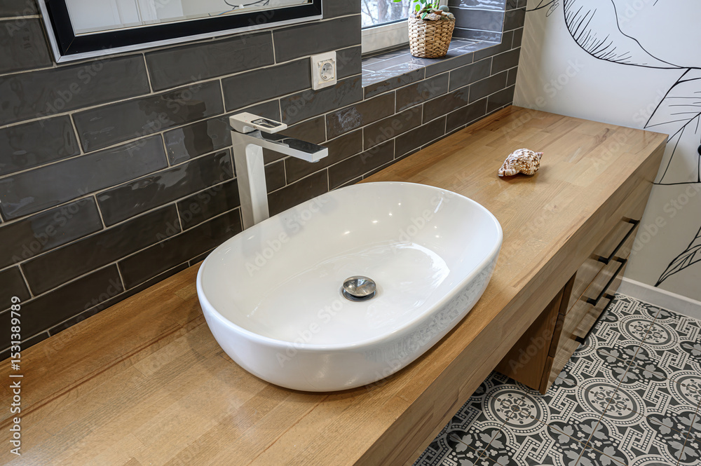 Fototapeta premium modern bathroom featuring a white oval sink, wooden countertop, and patterned tile floor. Dark grey brick-style tiles cover the wall