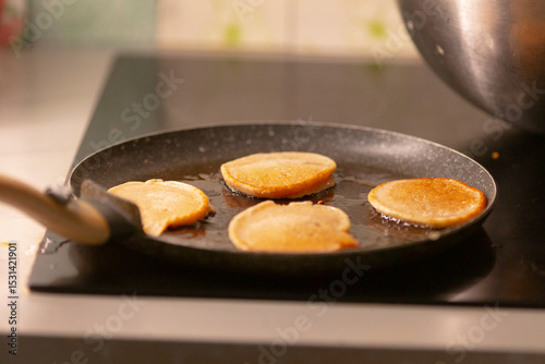 Pancakes are currently cooking on a frying pan situated on the stovetop in the kitchen, showcasing the delightful process of preparing a delicious breakfast food for your taste buds