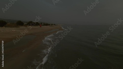Aerial view of small waves hitting the sandy beach during a dramatic cloudy sunset near Rethimno, Crete, Greece with soft light reflecting on the sea surface