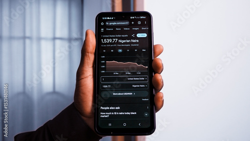 Accra, Ghana - June 12, 2025: Exchange rate of US dollars to Nigerian naira results on google search on mobile phone screen. Close up of person Hand holding smart phone showing financial chart in room