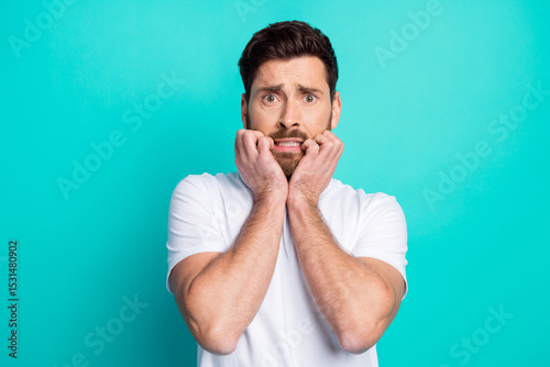 Young man expressing nervousness with his hands on face and a turquoise background, conveying anxiety and tension