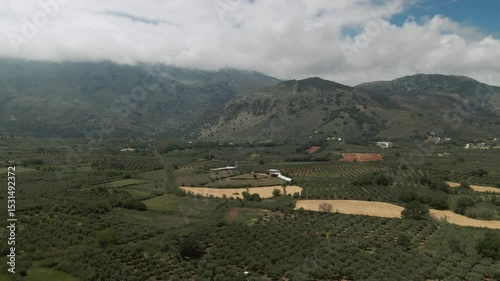 Aerial view of cultivated olive groves, patchwork fields, small farms and a dramatic cloud-covered mountain range in Asprouliani, Crete, Greece