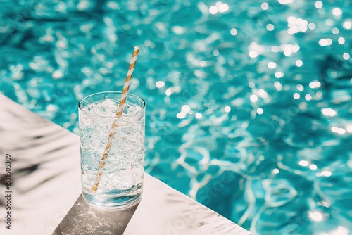 Glass of Iced Tropical Drink on Poolside Ledge with Turquoise Water and Sunlight Reflections