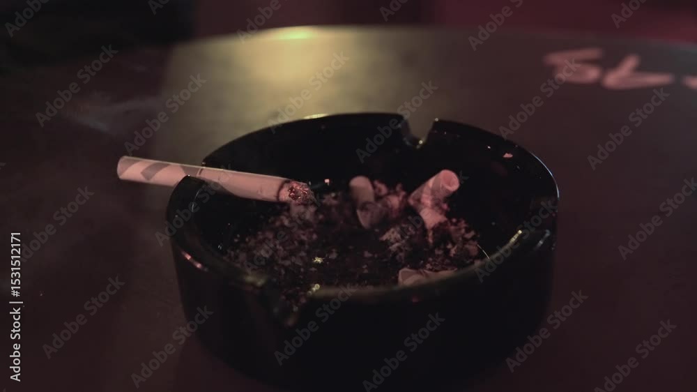 Lit burning cigarette resting in an ashtray on a dimly lit table in restaurant or caffee