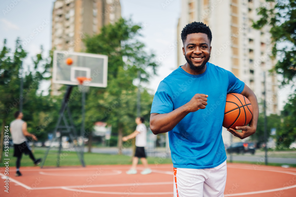 Smiling basketball player holding ball on outdoor court Smiling basketball player holding ball on outdoor court
