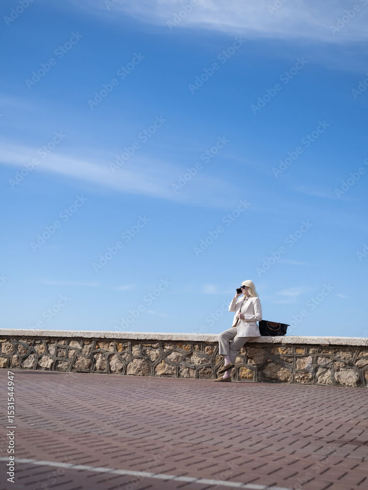 Obraz premium Businesswoman making a phone call on a stone wall under blue sky