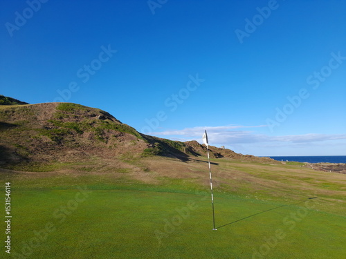 The hardest Par 3 in Britain, The Rockies, on Anstruther golf club in Scotland. The beautiful scenery filled with greenery and under a cloudless sky. The pin the hole with the flag blowing in the wind
