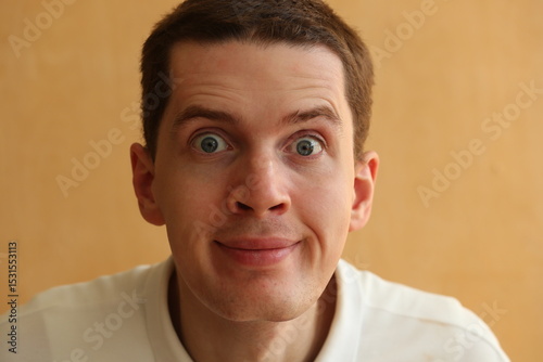 Emotional young man face with big surprised eyes on a light brown background.