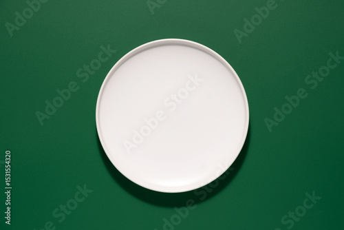 Empty round white plate on green background ready for serving food or appetizers during a meal
