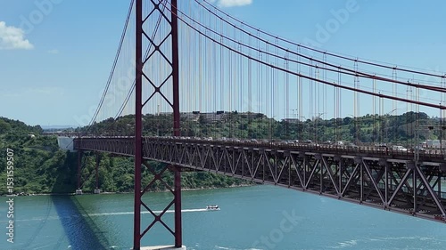 Urban drone flight under the iconic 25 de Abril Bridge in Lisbon, Portugal. Aerial scene capturing the structure’s scale, water reflections, and vibrant city energy from a dynamic, low-angle view.


