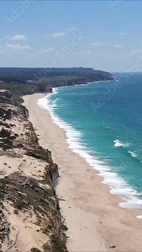 High drone view of Caparica beach near Lisbon, Portugal. Vehicle tracks drawn in the sand meet soft Atlantic waves. Aerial shot showing natural patterns and contrast between land and sea.

