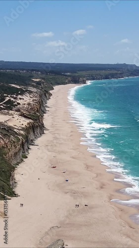 High drone view of Caparica beach near Lisbon, Portugal. Vehicle tracks drawn in the sand meet soft Atlantic waves. Aerial shot showing natural patterns and contrast between land and sea.

