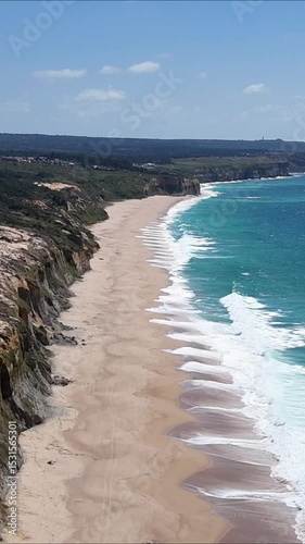 High drone view of Caparica beach near Lisbon, Portugal. Vehicle tracks drawn in the sand meet soft Atlantic waves. Aerial shot showing natural patterns and contrast between land and sea.

