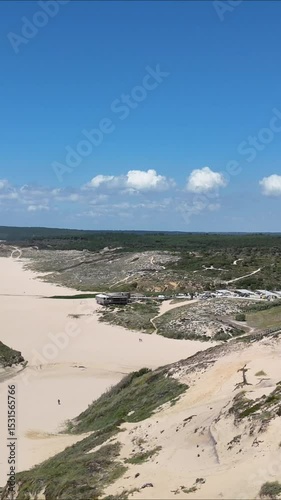 Drone shot starting over vast sandy terrain and moving toward the Portuguese coastline. Smooth transition from dry dunes to ocean view, blending textures of land and sea under natural light.

