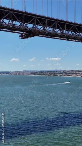 Urban drone flight under the iconic 25 de Abril Bridge in Lisbon, Portugal. Aerial scene capturing the structure’s scale, water reflections, and vibrant city energy from a dynamic, low-angle view.

