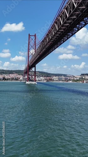 Urban drone flight under the iconic 25 de Abril Bridge in Lisbon, Portugal. Aerial scene capturing the structure’s scale, water reflections, and vibrant city energy from a dynamic, low-angle view.

