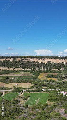 Drone turning from beach to inland cliffs and green terrain. Flying toward textured rock formations and coastal vegetation under soft natural light. Dynamic approach with cinematic depth and contrast.