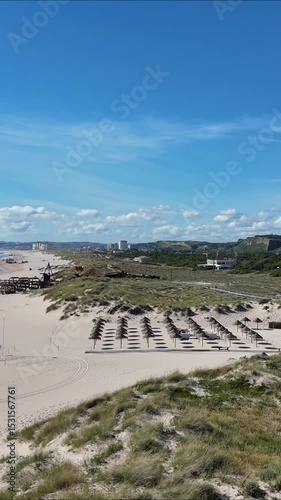Drone approaching a straw parasol on the sandy beach of Caparica near Lisbon, Portugal. Blue sky, warm sunlight, relaxed atmosphere and gentle cinematic motion.