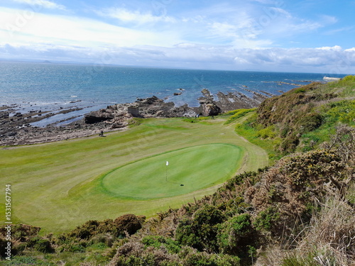A  view looking down of a well-kept, beautiful green in Anstruther, Fife, Scotland. The costal path visible in the background running alongside a rocky beach. In the foreground, some wild gorse.