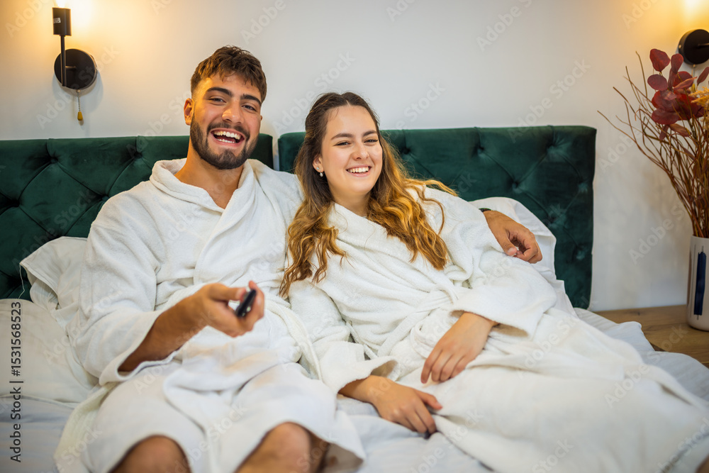 Obraz premium Relaxed Vacation Morning – Couple Watching TV in Bed
