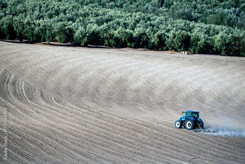 Tractor Plowing a Field with Olive Grove in the Background