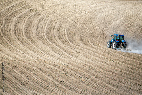A tractor moves across freshly plowed wavy soil, highlighting agricultural machinery and rural productivity in a minimalist landscape.