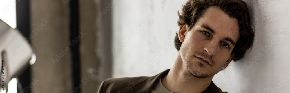 Obraz premium Banner. Young sexy handsome fit man in a brown suit looking at the camera sitting on a chair in the studio. Grey background, loft interior, studio. Causal stylish men's clothes, watch