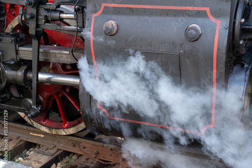 Steam engine generates plumes of vapor while in motion on a vintage railway during the afternoon