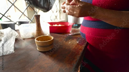 Skilled female cook peeling fresh garlic cloves using wooden mortar, working in rustic kitchen with traditional culinary techniques