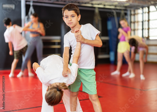 Teenage girl learns a hand grip in sparring with a boy during a workout. Children practice self-defense techniques in the gym