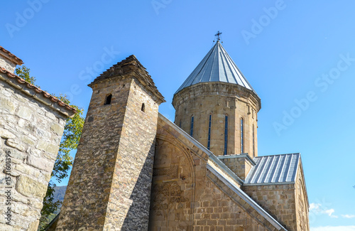 Historical Church of Virgin with stone walls and conical dome stands at the territory of Ananuri fortress under a blue sky. Georgia photo