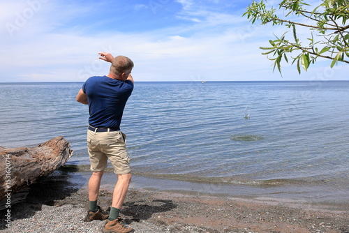 Middle-aged man in a blue shirt skips stones into a smooth blue lake