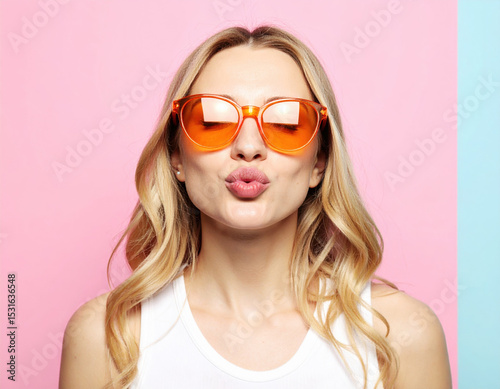 Pretty lady with orange sunglasses making playful kissy face against colorful background, radiating joy and confidence
